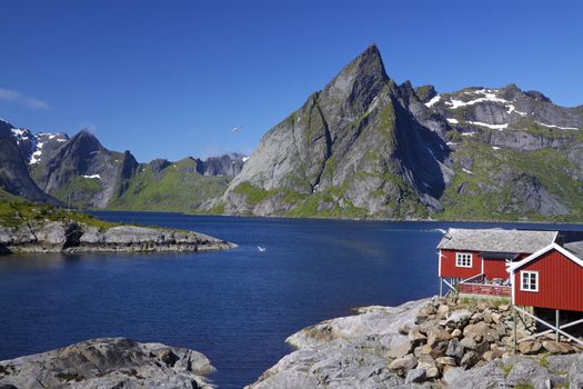 Scenic fjord on Lofoten islands with typical red fishing hut and towering mountain peaks