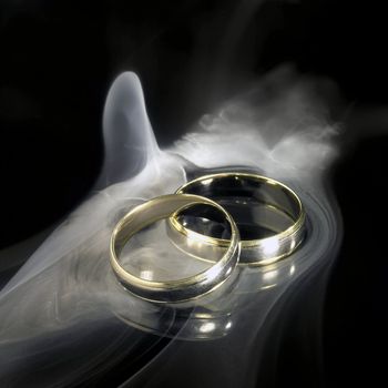 studio photography of two golden wedding rings and smoke in black reflective back
