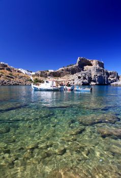 Emerald water at beautiful St Pauls Bay shadowed by the temple and castle ruins at Lindos 