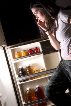A sleepy woman lingers at the refrigerator door