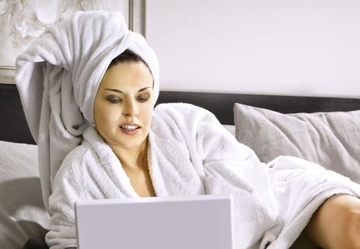 beautiful woman in white bathrobe on a bed with laptop