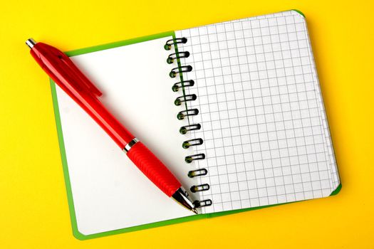 Opened notebook squared pagewith red pen over it on yellow background 