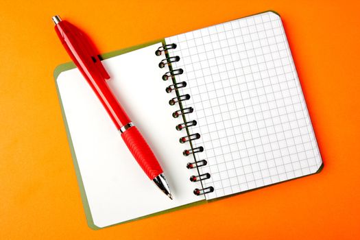 Opened notebook squared pagewith red pen over it on orange background 