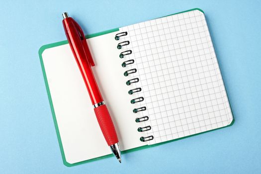 Opened notebook squared pagewith red pen over it on blue background 