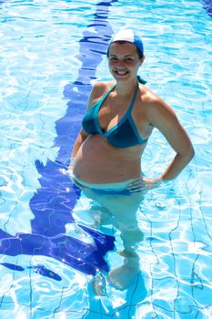 Good looking woman pregnant inside swimmingpool standing happy relaxed