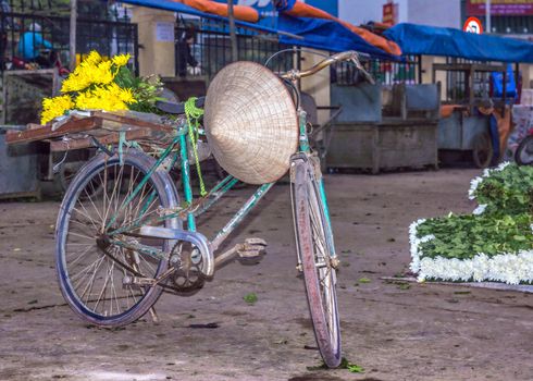 Blue green bike holds yellow flowers with white flowers on the side.