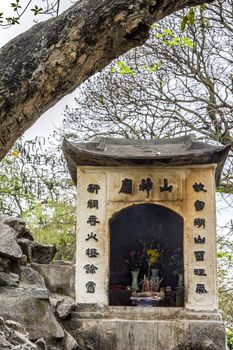 Old stone construction with chinese characters under tree.