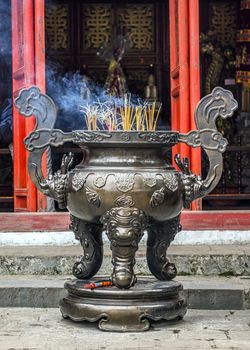 Vietnam Hanoi. Decorated heavey metal receptacle against red framed background.