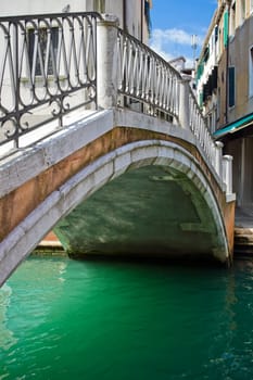 Nice stone bridge over green water of a venetian canal, Italy