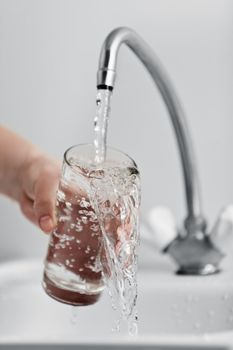 Human hand holding glass pouring fresh drink water at kitchen faucet