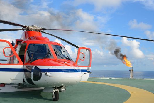 The helicopter park on oil rig to pick up worker with gas flare and blue sky backgroung