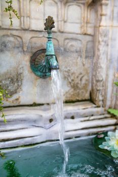 Old marble fountain with brass faucet still pouring water.