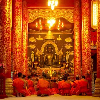 Group of buddhist monks sitting in the temple and praying