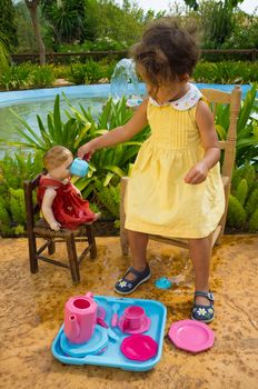 Small girl giving her old doll a cup of tea