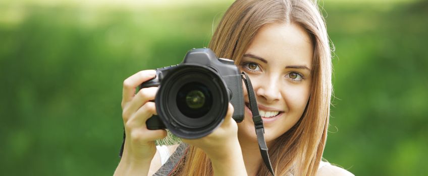 Portrait of beautiful smiling blonde girl , making photos at summer green park.