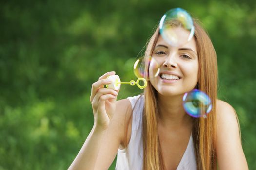 Beautiful young woman smiling and blowing bubbles outdoor in the nature.