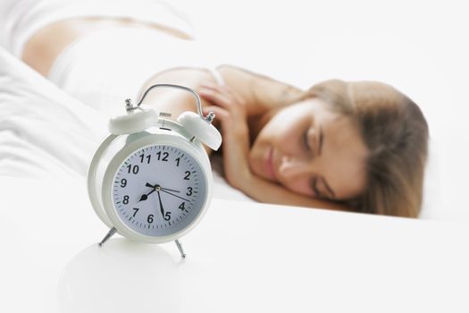 A young lady sleeping on the background with a clock on the foreground.