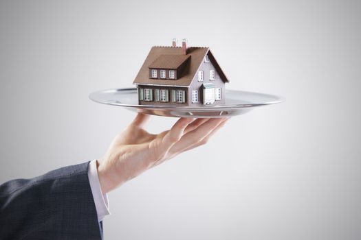 Real estate offer. Businessman holding a silver tray with an artificial model of the house