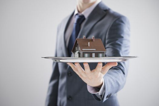 Real estate offer. Businessman holding a silver tray with an artificial model of the house