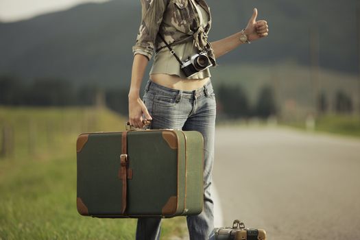 A woman hitchhikes on the side of the road.