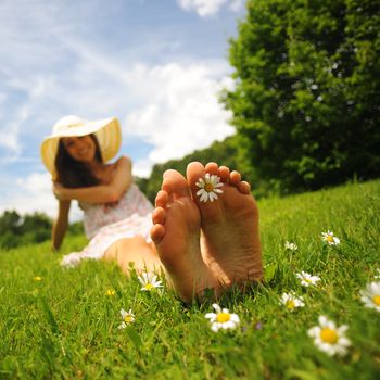 a smiling young woman is lying on a green lawn, with a daisy between her toes; shallow deep of field
