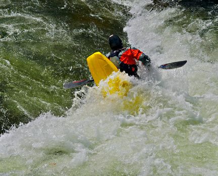 A man kayaking in the rapids at a rock, practicing turns.