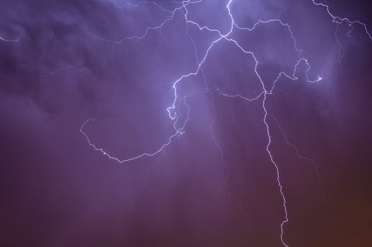 Bright dramatic lightening stretched across the night sky over a cities ambient orange glow of lights giving it unique colors