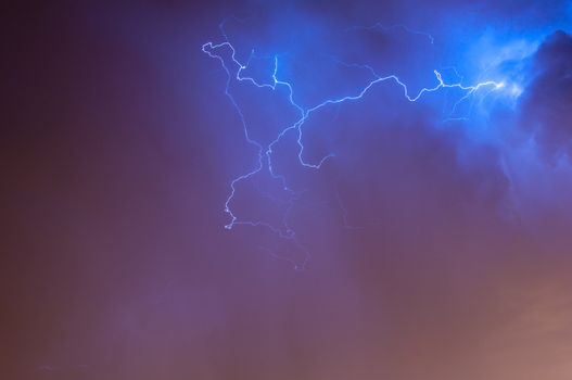 Bright dramatic lightening stretched across the night sky over a cities ambient orange glow of lights giving it unique colors