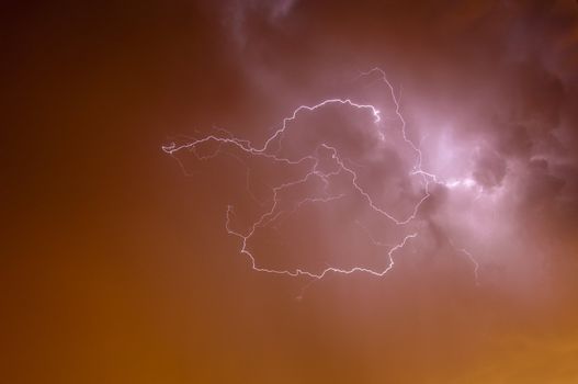 Bright dramatic lightening stretched across the night sky over a cities ambient orange glow of lights giving it unique colors