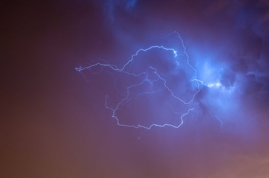 Bright dramatic lightening stretched across the night sky over a cities ambient orange glow of lights giving it unique colors