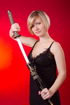 Young beautiful blonde girl holding sword on red background. 