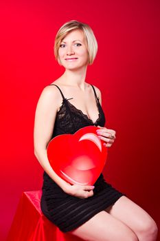 Young beautiful blonde girl hugs a big heart. Feast of St. Valentine's Day. 