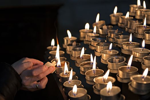 A womand lights candles in a church while her child put his hand on hers.