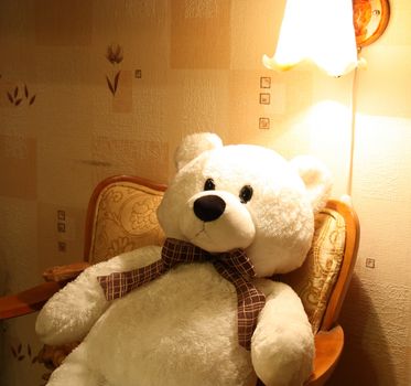 Teddy bear sitting in the armchair in the night waiting for his friend back home