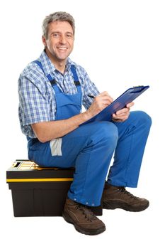 Confident service man sitting on toolbox and taking notes. Isolated on white