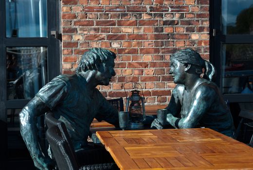 Sculpture of man and woman sitting at table in bar, Oslo.