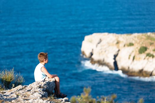 Young kid peacefully watching the waves of Black Sea. He is high sitting on the rocks.