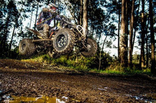 Quad rider jumping on a muddy forest trail.