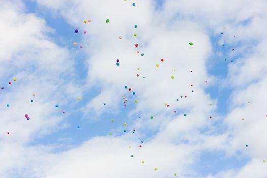 many colorful balloons high in the blue sky with white clouds