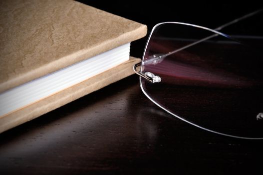 Eyeglasses next to a book on top of a wood table