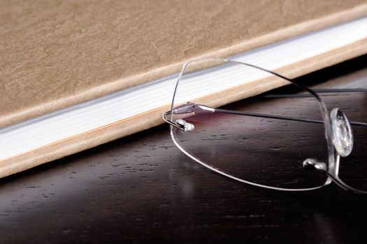 Eyeglasses next to a book on top of a wood table