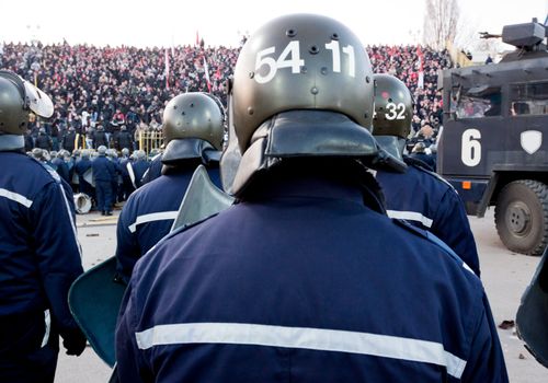 Back of policeman with helmet guarding red football fans