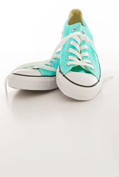 Pair of turquoise and white sneakers with laces on a blank background
