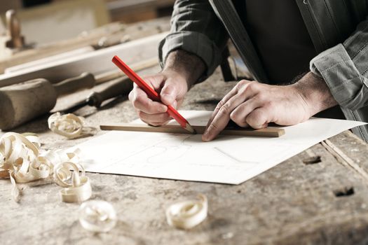 Closeup  view of a carpenter using a red pencil to draw a line on a blueprint