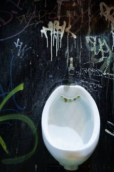 Old grungy white urinal against graffitis wall