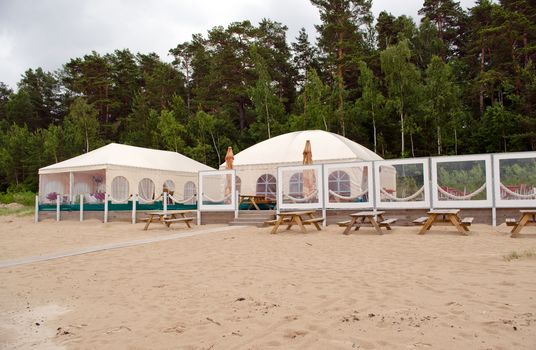 Restaurant bar tents on seaside sand. Wooden outdoor table and bench.