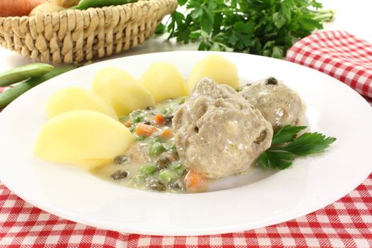 cooked meatballs in a white sauce with capers and potatoes on a bright background