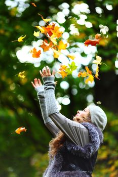 woman drop up leaves in autumn park