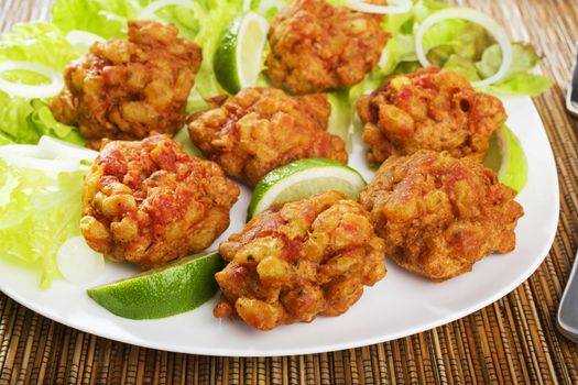 Favourite Indian appetizer, Indian bhajias or bhajis, on a white plate with sliced lime and lettuce.