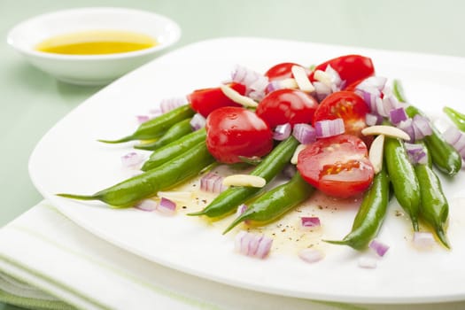 Salad of green beans, tomatoes, red onion, almonds  and lemon vinaigrette, arranged on a white plate.